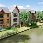 Canal-side wooden apartments with trees and sky.