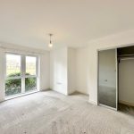Empty bedroom with large window and mirrored wardrobe.
