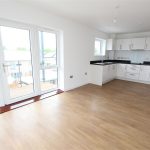Modern kitchen with wooden floors and large windows.