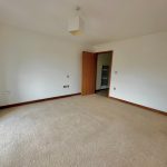 Spacious empty room with beige carpet and open door.