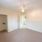 Empty beige bedroom with open closet and ceiling fan.