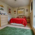 Cosy bedroom with red bedding and green rug.