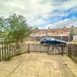Gated courtyard garden with parked cars in background.