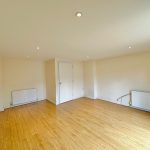 Empty room with wooden flooring and radiators.