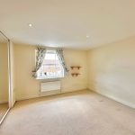 Spacious bedroom with mirrored wardrobe and window.
