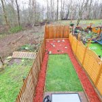 Back garden with fences and grass, wooded area beyond.