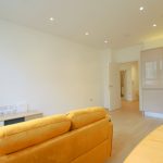 Modern open-plan living room with yellow sofa and kitchen.