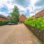 Brick houses and leafy driveway under cloudy sky.