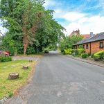 Quiet suburban street with trees and brick houses.