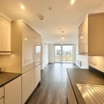 Modern kitchen with wood flooring and large windows.