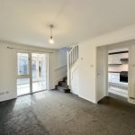 Empty room with staircase and kitchen view.