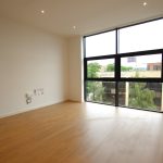 Empty room with large window and hardwood floor.