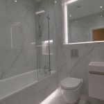 Modern white tiled bathroom with bathtub and toilet.