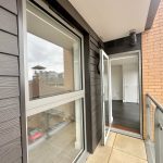 Modern balcony with open door and city view.