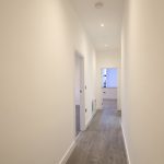 Long, bright hallway with wooden floors and white walls.