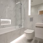 Modern marble bathroom with bathtub and mirror lighting.