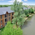 Modern apartments beside tranquil canal surrounded by trees.