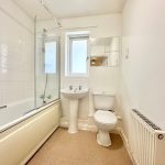 Small white bathroom with bathtub and window.