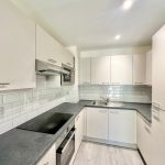 Modern white kitchen with appliances and tiled backsplash.