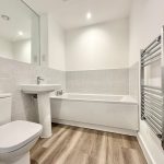 Modern bathroom with white fixtures and wood flooring.