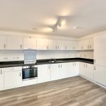 Modern white kitchen with wooden floor and appliances.