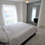 Modern bedroom with large window and mirrored wardrobe.