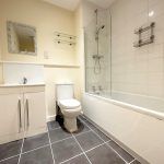 Modern bathroom with bath, sink, toilet, and mirror.