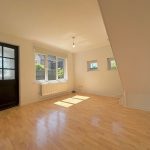 Bright empty room with wooden flooring and windows.