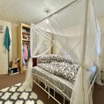 Cosy bedroom with canopy bed and open wardrobe.