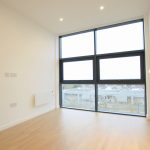 Empty room with large window and wooden floor.