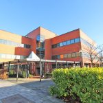 Modern red-brick office building in bright sunlight.