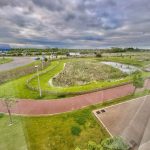 Green landscape with pond and paths under cloudy sky.