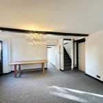 Spacious room with table, chandelier, and staircase.