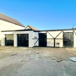 Detached garage block with black doors, sunny day.
