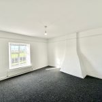Bright unfurnished room with window and grey carpet.