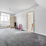 Spacious grey-carpeted room with wicker chair and door.
