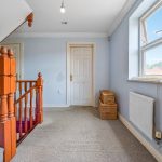 Carpeted landing with wooden banister and large window.