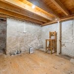 Basement room with exposed beams and stone walls.