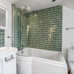Modern bathroom with green tiled walls and glass shower.