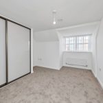 Empty carpeted room with large window and wardrobe.
