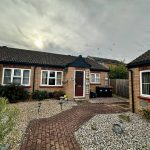 Brick bungalow with pebbled front garden under cloudy sky.