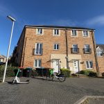 Three-storey brick house with parked scooter and bicycle.