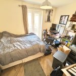 Cosy bedroom with bed, desk, and shelves.