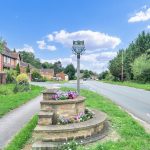 Village road with flower display and signpost.