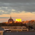 Sunset reflecting on cityscape buildings and church dome.