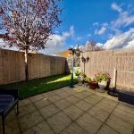 Sunny garden with patio and potted plants.