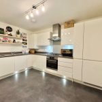 Modern white kitchen with shelves and lighting.
