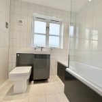 Modern white tiled bathroom with bathtub and window.