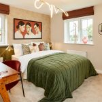 Cosy bedroom with desk, artwork, and green bedspread.