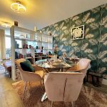Stylish dining area with tropical wallpaper and pink chairs.